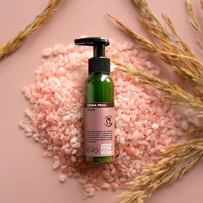 immagine prodotto crema piega ambientata  su sfondo rosa decorata con foglie verdi e sale rosa 